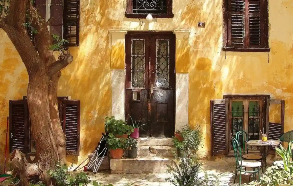 Ochre-colored neoclassical house facade in Athens with plants on the front steps