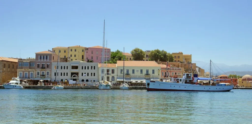 Wide-angle view of the historic Chania harbor in Crete on a bright sunny day with a traditional boat moored on the right.