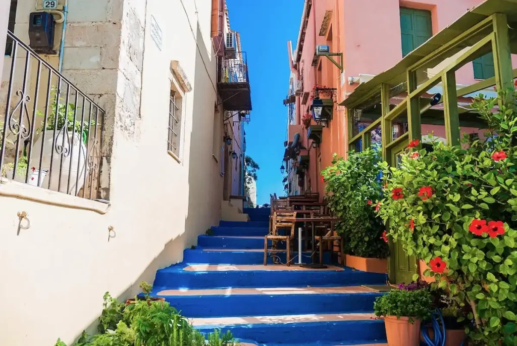 Vibrant alleyway in Rethymno featuring indigo blue stairs, olive green window frames, and a peach-colored mansion wall.