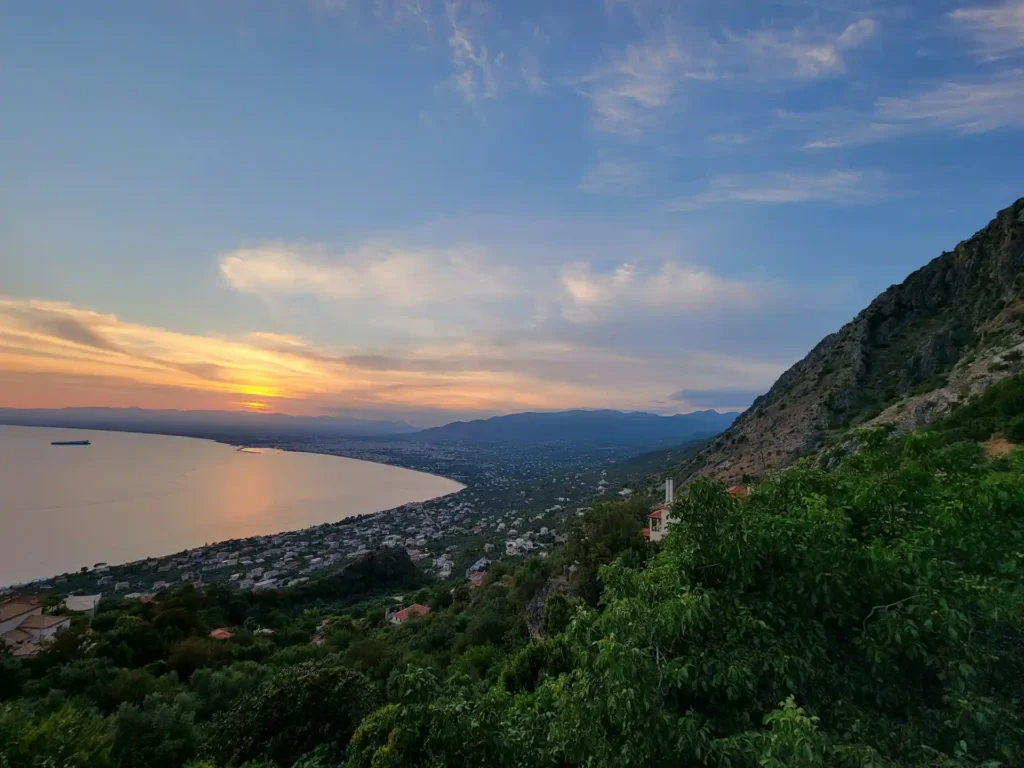 View from above Kalamata at sunset, overlooking the town, coastline, and beach under a colored sky
