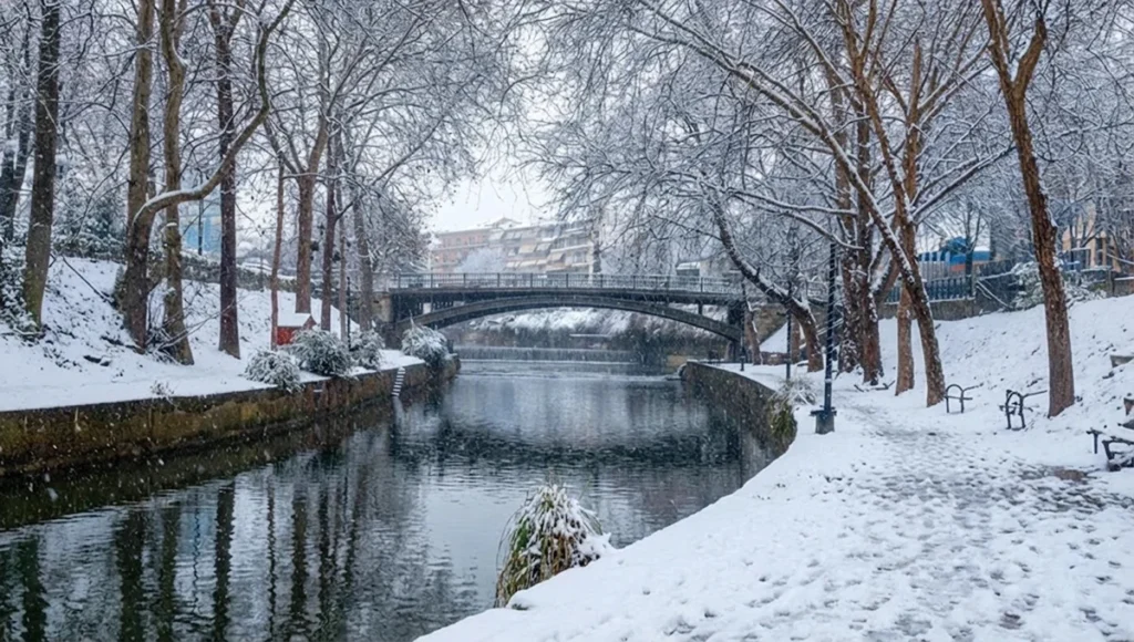 The iconic stone bridge crossing the Litaios River in Trikala, surrounded by lush trees and city life.