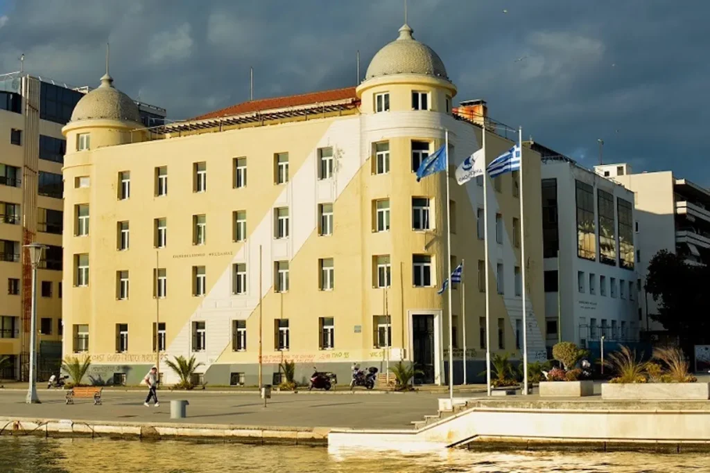 The grand, multi-story historic Papastratos tobacco warehouse on the Volos seafront, featuring industrial brick and stone architecture, now serving as the University of Thessaly administration.