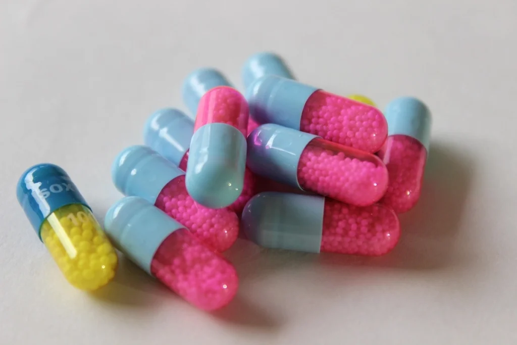 A close-up, top-down shot of a scattering of bright pink and light blue medicinal pills on a flat surface.