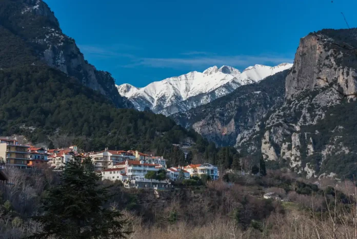 Aerial view of Litochoro town clustered at the foot of Mount Olympus with the Enipeas Gorge cutting into the green slopes behind it.