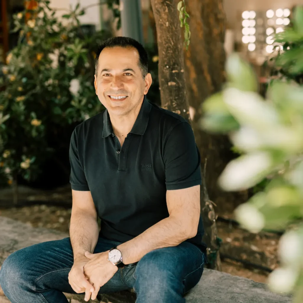 Thessaloniki city councilor Spiros Pengas sitting on a dry-stone bench in central Thessaloniki wearing a dark polo shirt and jeans.