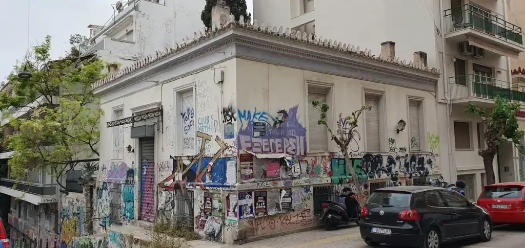 A one-story neoclassical house in Exarcheia, its façade covered in graffiti, with the dominant tag reading "ΕΞΕΓΕΡΣΗ" (rebellion) at the center.
