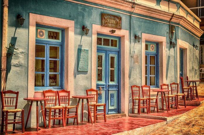Traditional Greek kafeneio exterior with red chairs, blue-shuttered windows and turquoise walls.