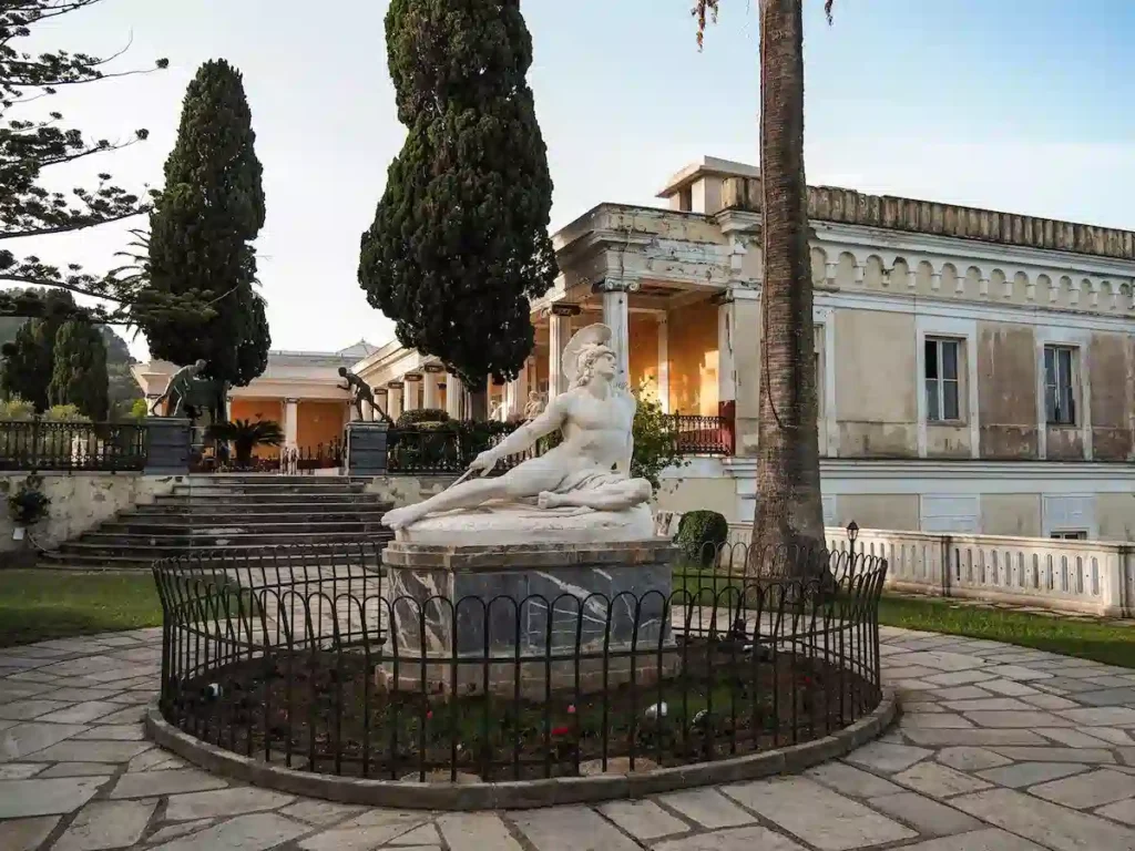 Exterior view of the neoclassical Achilleion Palace with stone statues and landscaped gardens in Gastouri, Corfu.