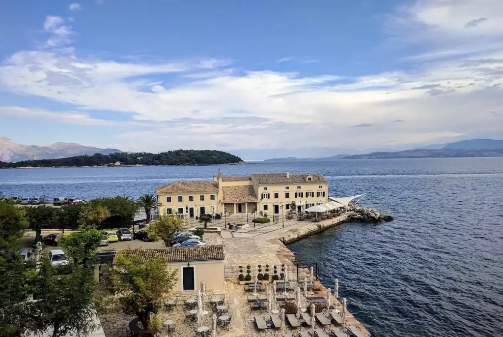 Faliraki Beach in Corfu Town with clear blue water and historic coastal buildings in the background.