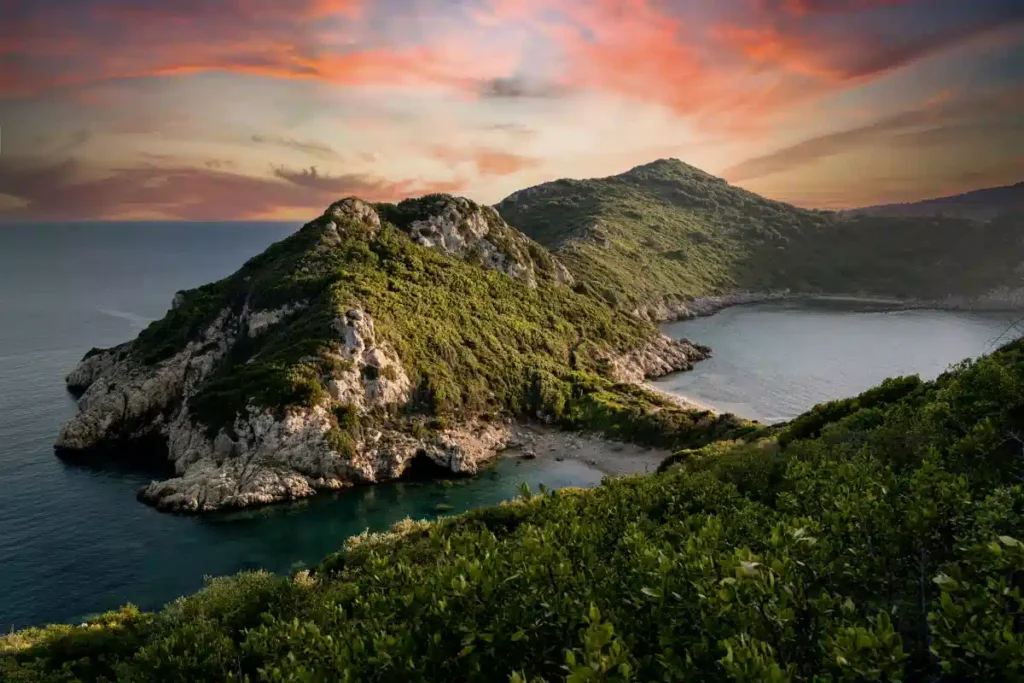 Lush green rocky peninsula forming a sheltered lagoon under warm golden sunset light in Corfu