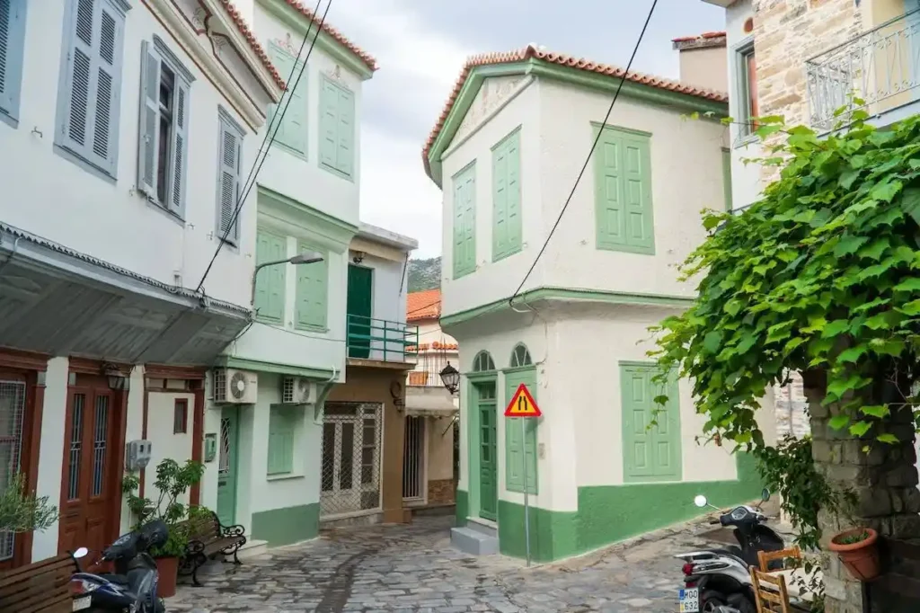 A quiet pedestrian street in Samos featuring traditional old buildings with colorful green and light blue window frames and doors.