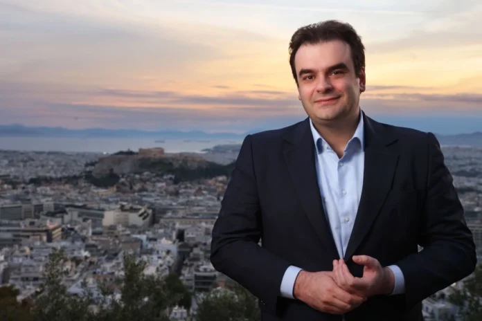 Kyriakos Pierrakakis, MP for Athens A, standing on a hill in Athens with the Parthenon and the coast in the background.