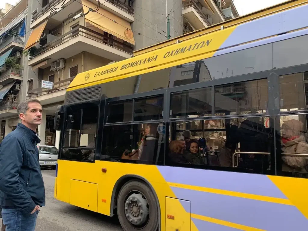 A trolley bus on a Koukaki street alongside a former mayor standing nearby.